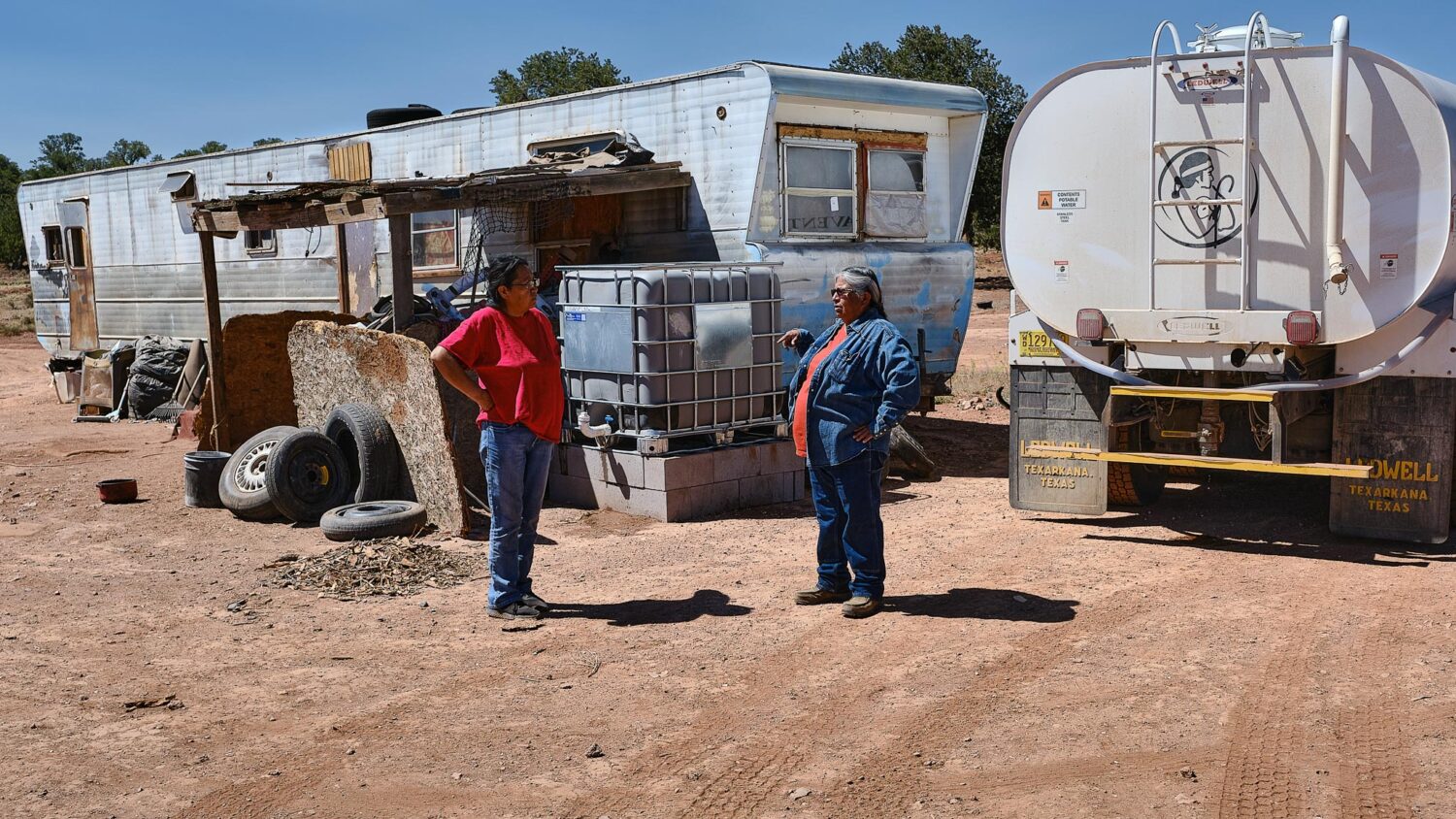 Darlene and neighbor talk while Darlene delivers water to her house.