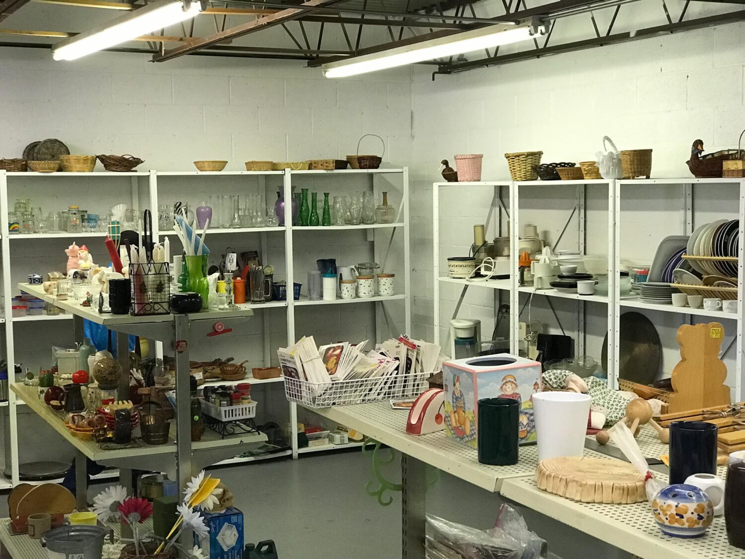Inside of thrift store, with several white shelves displaying household items, including decorative items like baskets.