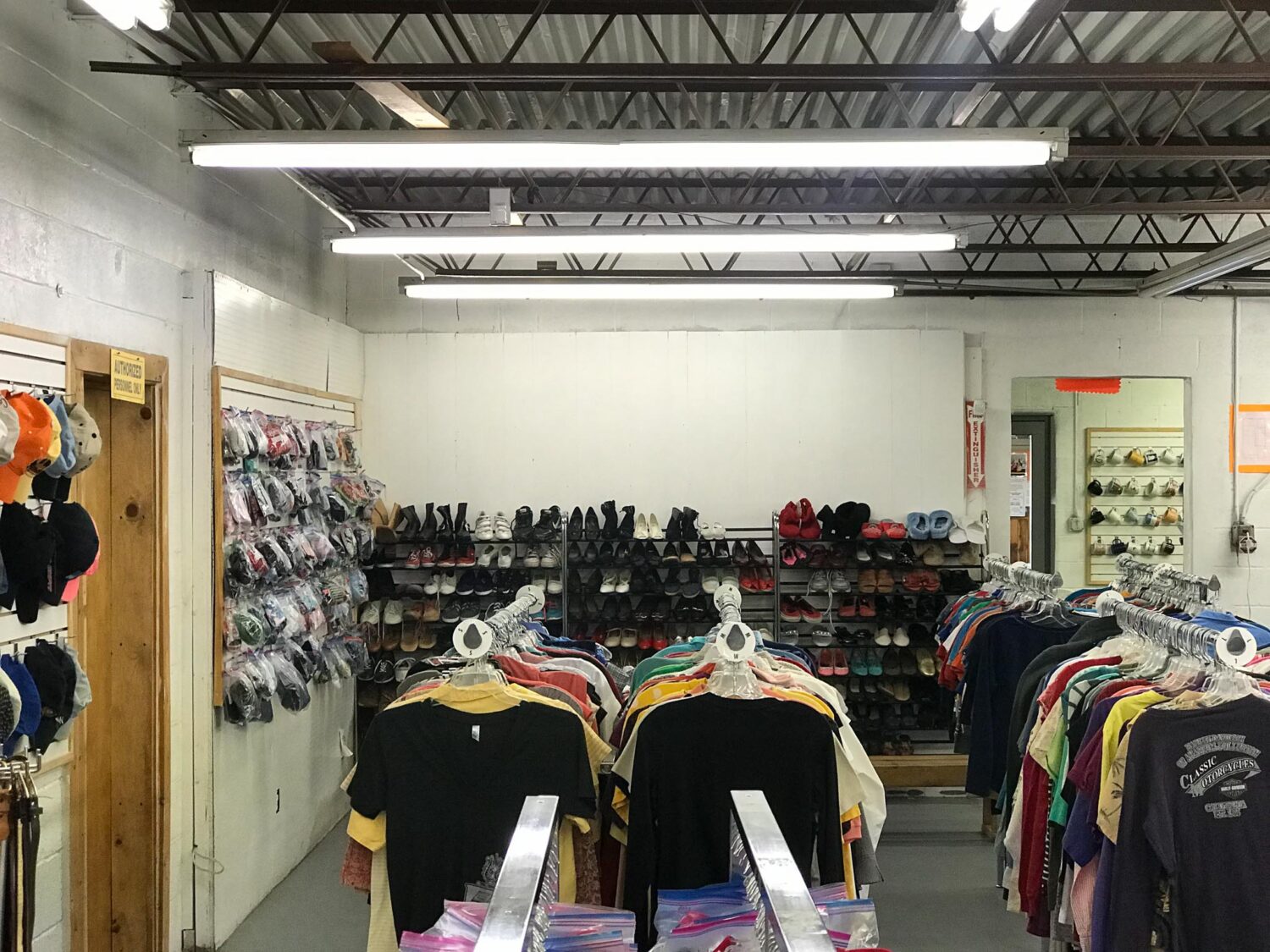 Inside of thrift store, with several racks of clothing like shirts, shoes, and hats.